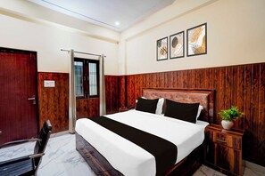 A hotel room with a wooden headboard, a bed with black and white bedding, a bedside table with a plant, and a window with bars. - Super Townhouse Matiyari (Lucknow)