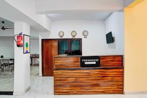 A reception desk labeled 'TOWNHOUSE' with a company-serviced sign, a fire extinguisher, and three clocks on the wall. - Super Townhouse Matiyari (Lucknow)