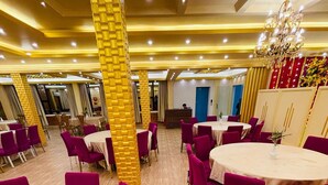 Un comedor de hotel con mesas redondas, sillas moradas y una araña.