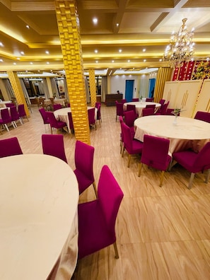 Une salle à manger d’hôtel avec des tables rondes, des chaises violettes et un lustre.