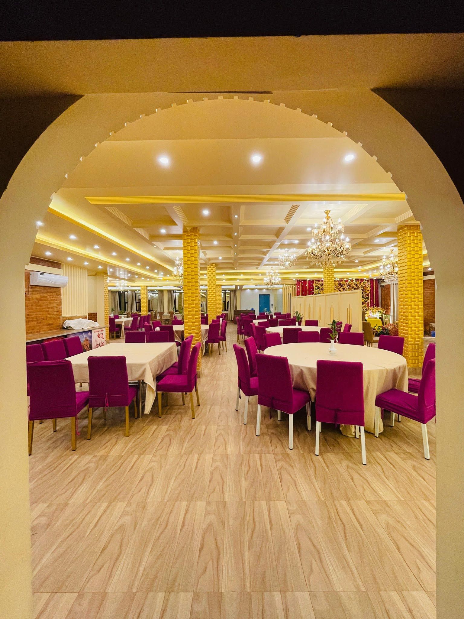 Un restaurante con mesas redondas y sillas moradas, un candelabro y una pared de ladrillo.