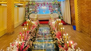 Habitación de hotel con un largo pasillo decorado con arreglos florales, dos sofás y una araña.