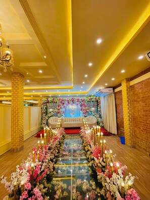 Une chambre d’hôtel avec un long couloir bordé de compositions florales, deux canapés et un lustre.