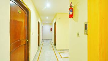 A hallway with wooden doors, a fire extinguisher mounted on the wall, and a tiled floor.