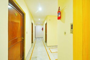 A hallway with wooden doors, a fire extinguisher mounted on the wall, and a tiled floor.