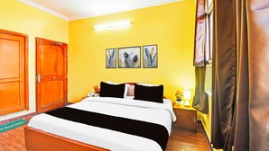 Quarto de hotel com cama, mesa de cabeceira, luminária, janela com cortinas e porta.
