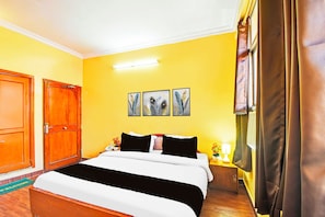 A hotel room with a bed, a nightstand, a lamp, a window with curtains, and a door. - Townhouse Hathroi Market (Jaipur)