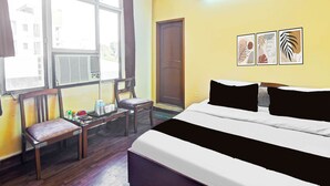 Quarto de hotel com cama, escrivaninha, cadeira, janela e obras de arte na parede.