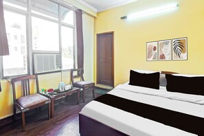 A hotel room with a bed, a desk, a chair, a window, and artwork on the wall. - Townhouse Hathroi Market (Jaipur)