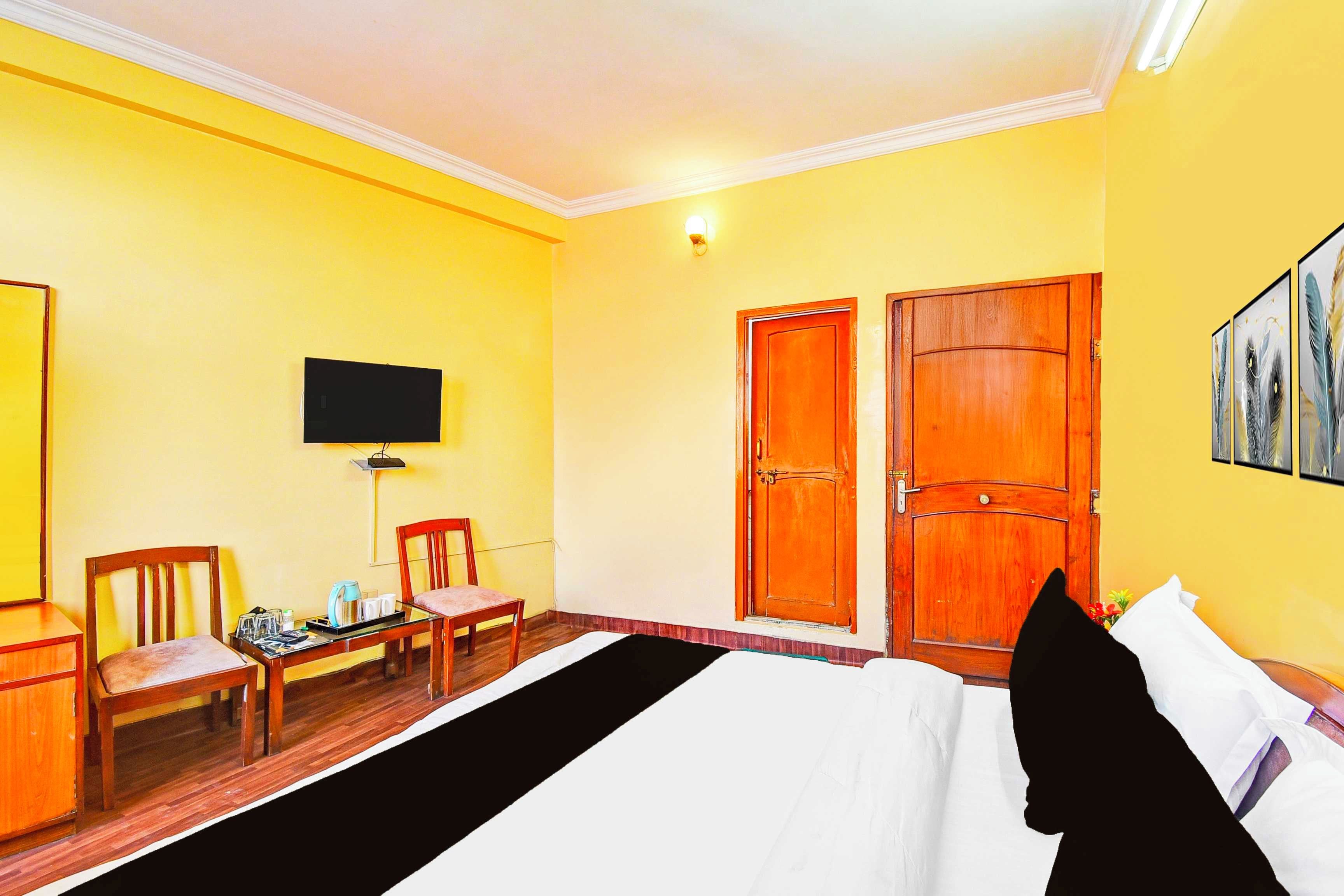 Habitación de hotel con una cama, dos puertas de madera, un televisor en la pared y una pequeña mesa con sillas.