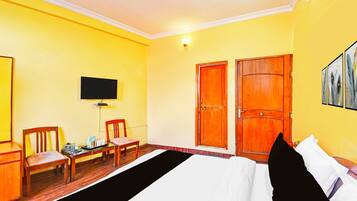 A hotel room with a bed, two wooden doors, a television on the wall, and a small table with chairs.