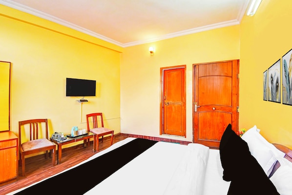 A hotel room with a bed, two wooden doors, a television on the wall, and a small table with chairs.