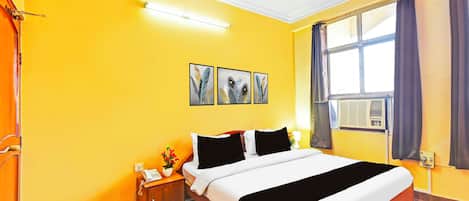 Quarto de hotel com cama, mesa de cabeceira com telefone, janela com cortinas e três peças de arte de pena na parede.