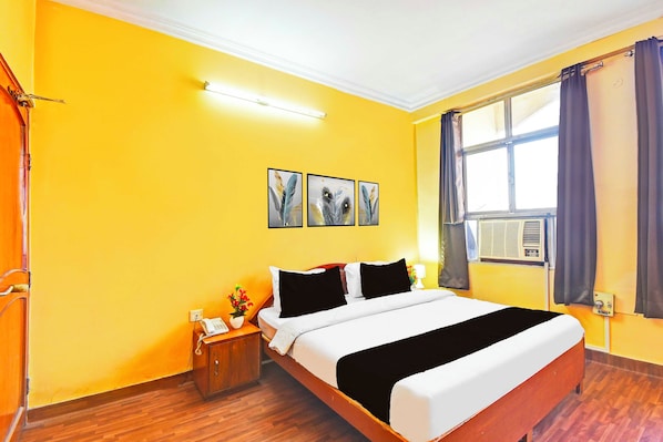 A hotel room with a bed, a bedside table with a telephone, a window with curtains, and three feather wall art pieces.