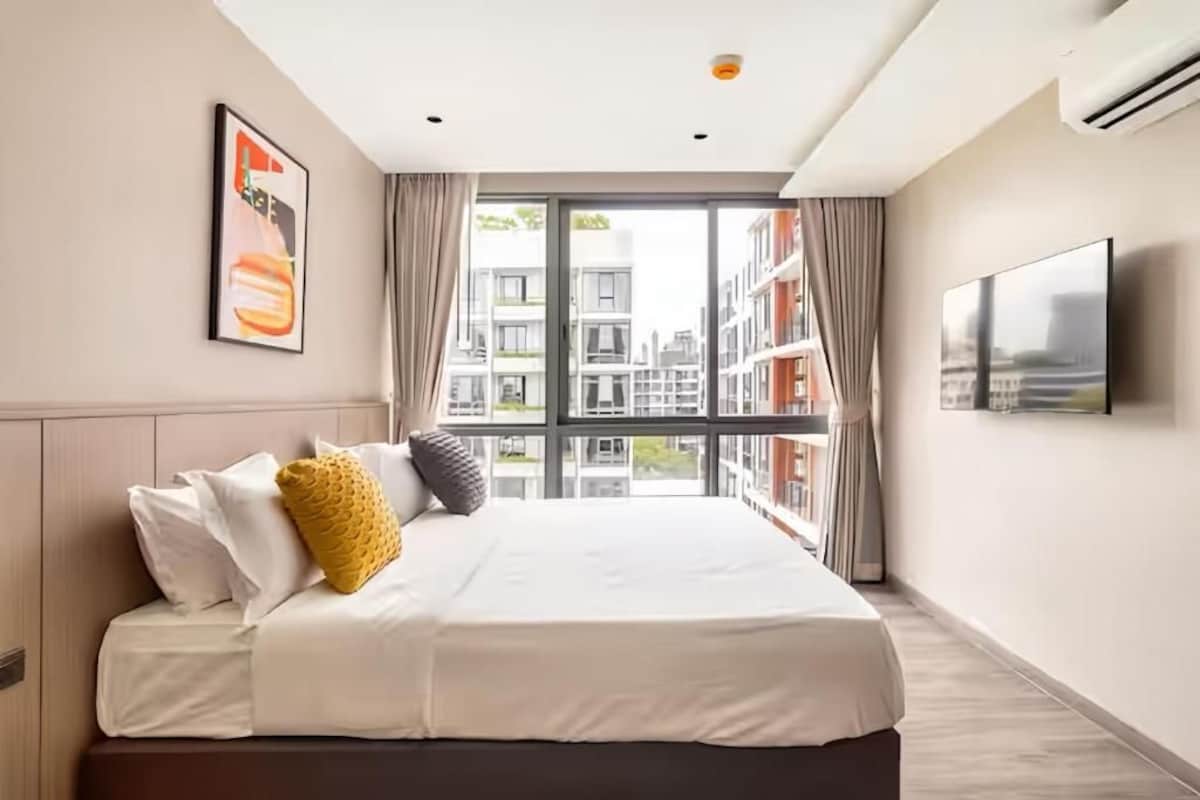 A hotel room with a large bed, a television, and a view of buildings through the window.