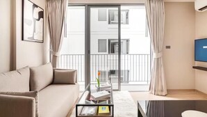 Un salon moderne avec un canapé, une table basse en verre et une vue sur un immeuble à travers une porte vitrée.