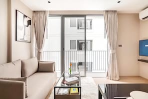 A modern living room with a sofa, a glass coffee table, and a view of a building through a glass door. - Tierra Residences in Bangkok (Krung Thep Maha Nakhon)