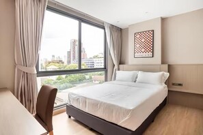 A hotel room with a large window, a bed, a desk, and a chair. - Tierra Residences in Bangkok (Krung Thep Maha Nakhon)