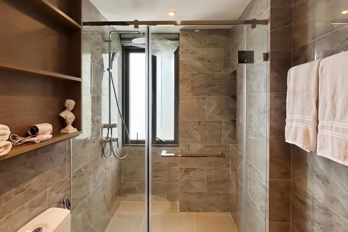 A modern bathroom with a glass-enclosed shower, marble tiles, and a towel rack.