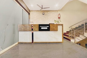A reception desk with a sign indicating company-serviced services, a ceiling fan, a staircase, and a brick wall. - Townhouse Oak Taj Nagri Phase 2 (Agra)