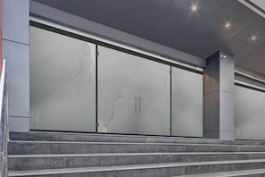 A modern building entrance with a glass facade, metal railings, and a series of steps leading up to the entrance. - Townhouse Oak Taj Nagri Phase 2 (Agra)