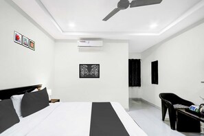 A modern hotel room with a bed, a desk, a chair, an air conditioning unit, and a ceiling fan. - Townhouse Oak Taj Nagri Phase 2 (Agra)