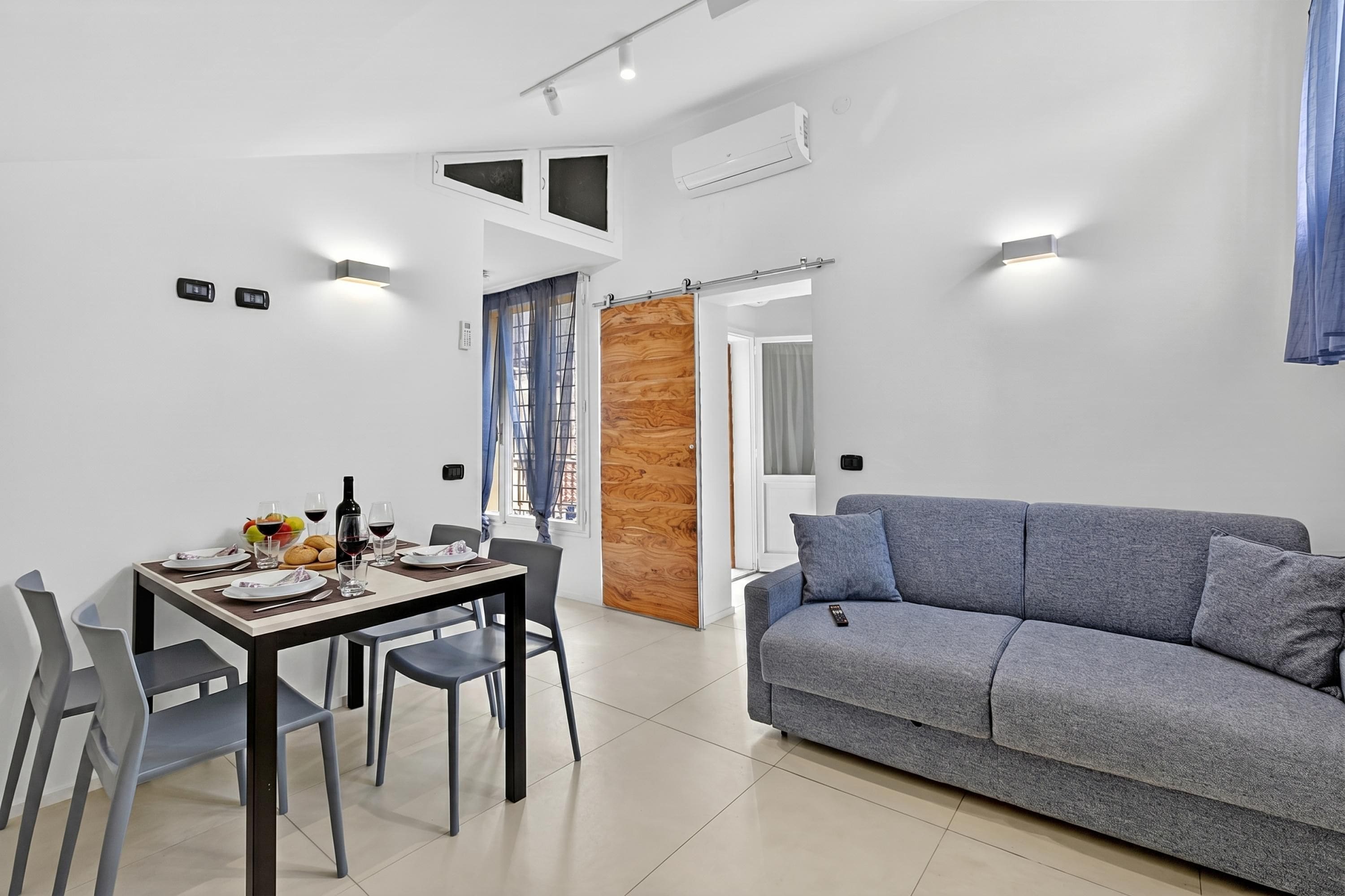 A modern living space with a dining area, a grey sofa, and a wooden accent wall.