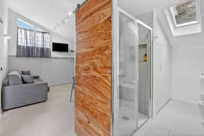 A modern interior with a grey sofa, a wooden accent wall, a glass shower enclosure, and a mounted TV. - Sant'eufemia 14 (Modena)