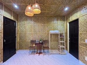 A room with a bamboo-patterned wall, a wooden table with chairs, a hanging light fixture, and a shoe rack.