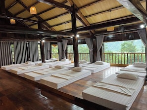 A room with multiple beds arranged in rows, wooden flooring, and a view of greenery outside. - Suoi Sapa Homestay And Trekking (Ta Van)