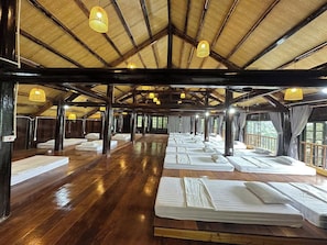 Amplia habitación con piso de madera y techo alto, con varias camas dispuestas en filas.