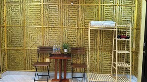 A room with a bamboo-patterned wall, a wooden table with chairs, a small shelf with towels, and a ladder. - Suoi Sapa Homestay And Trekking (Ta Van)