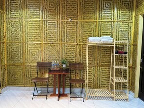 Una habitación con pared de bambú, una mesa de madera con sillas, un estante pequeño con toallas y una escalera.