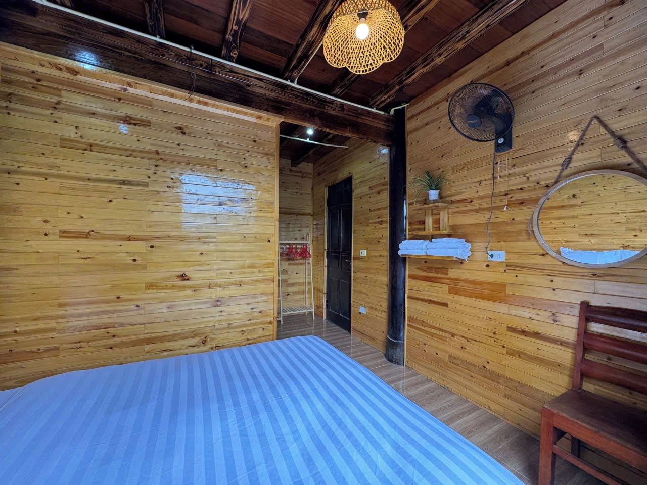 Habitació de cabana de fusta amb un llit, una cadira, un ventilador i un mirall a la paret.