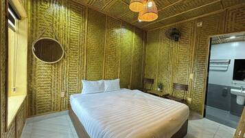 A room with a large bed, a round mirror, a wooden bench, and a bathroom with a sink and mirror.