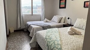 A hotel room with two beds, a window with curtains, a ceiling light, and a patterned floor. - CASA AZALEA (Ciudad de Guatemala)