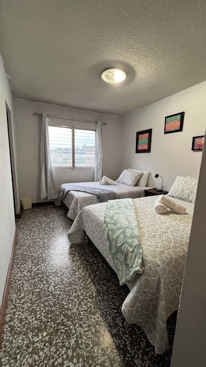 Habitación de hotel con dos camas, una ventana con cortinas, una lámpara en el techo y piso con diseño.