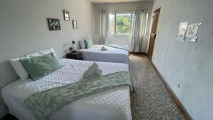 A hotel room with two beds, a window with curtains, a small table with a lamp, and a door. - CASA AZALEA (Ciudad de Guatemala)
