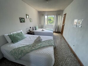 Habitación de hotel con dos camas, una ventana con cortinas, una mesita con lámpara y una puerta.