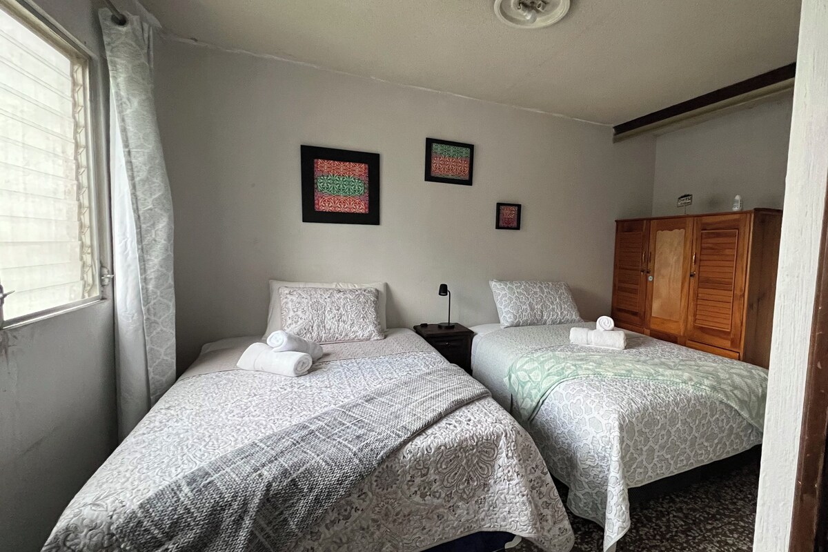 Una habitación con dos camas, un armario de madera y dos cuadros colgados en la pared.