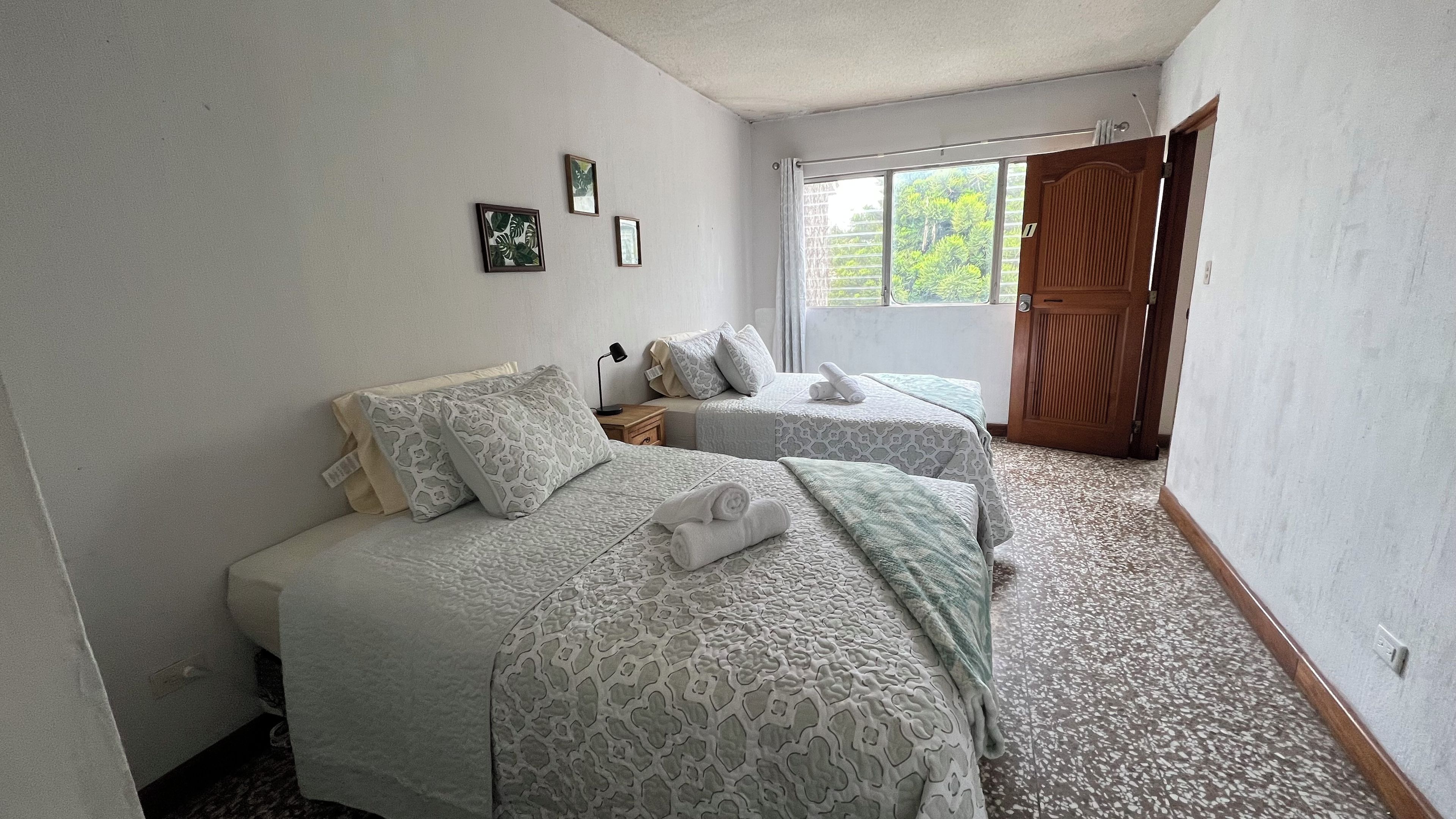 Un dormitorio con dos camas, una ventana con vistas a zonas verdes y una puerta.
