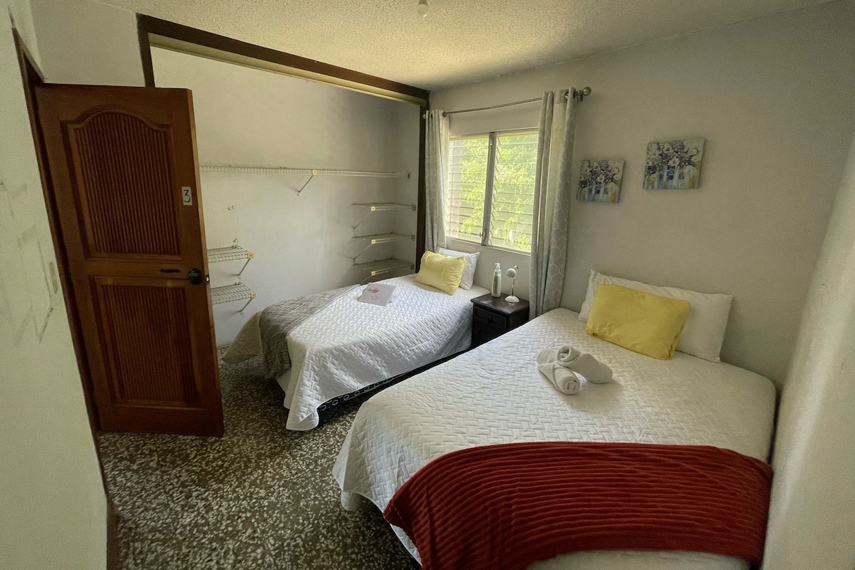 Un dormitorio con dos camas, una puerta, un ventanal y un estante fijado a la pared.