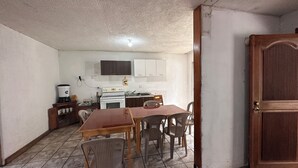 A compact kitchen with white cabinets, a stove, and a sink. There is a dining table with chairs and a wooden door. - CASA AZALEA (Ciudad de Guatemala)