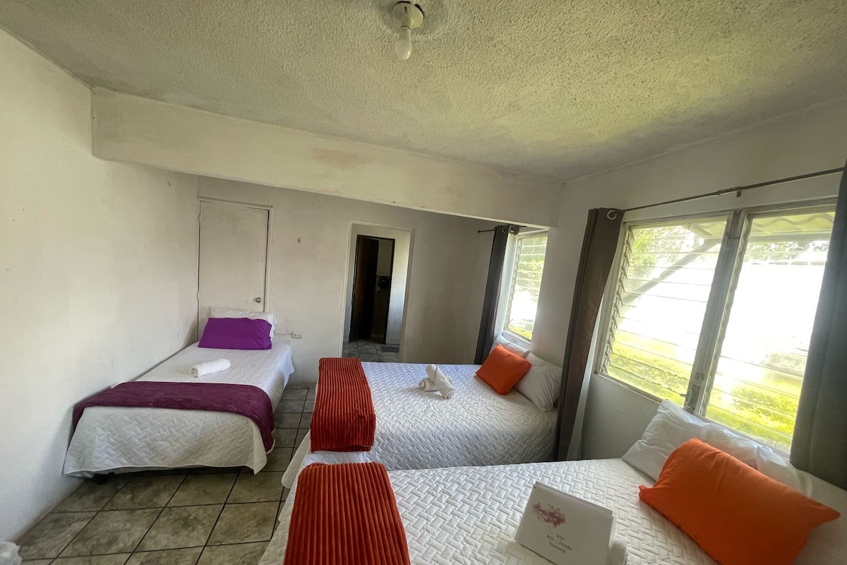 Habitación de hotel con dos camas, una ventana y una puerta que da a otra habitación.
