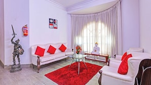 A living room with a white sofa, red cushions, a glass coffee table, a statue, a Buddha statue, and a fire extinguisher on the wall. - Townhouse Seethammadhara Junction (Visakhapatnam)