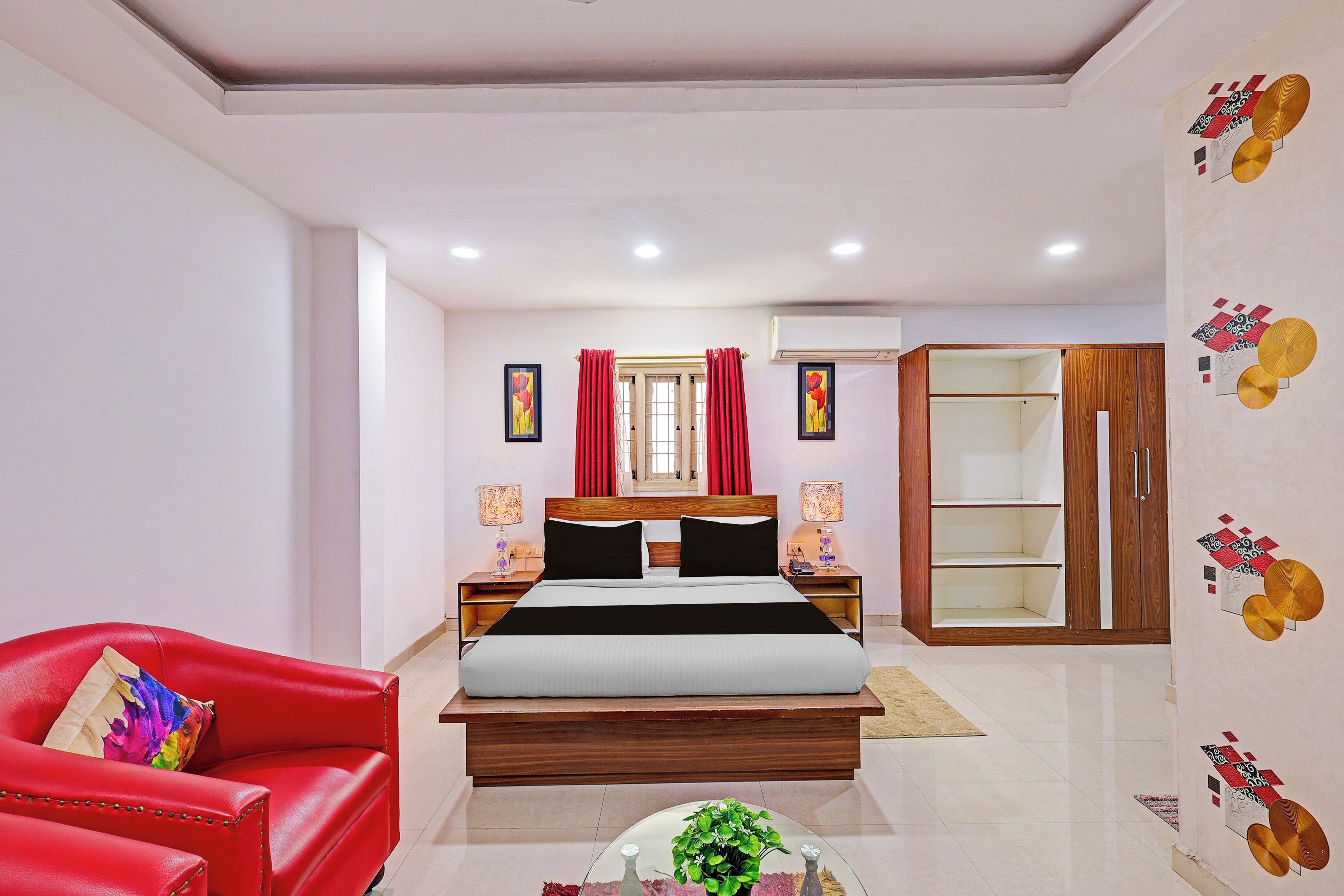 Quarto de hotel com cama, uma cadeira vermelha, mesa de cabeceira, guarda-roupa e parede com desenhos decorativos.