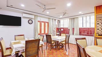 A dining area with a high ceiling, ceiling fans, a clock, and a large window with curtains.
