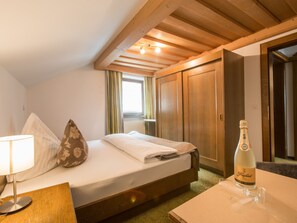 A hotel room with a bed, a bedside table with a lamp, a bottle of champagne, and a window with curtains. - Haus am Brunnen, (Samnaun-Compatsch) by Interhome (Samnaun)