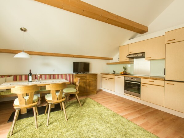A modern kitchen with wooden cabinets, a built-in oven, and a dining area with a table and chairs. - Haus am Brunnen, (Samnaun-Compatsch) by Interhome (Samnaun)