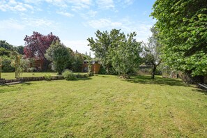 Ein gepflegter Garten mit Rasen, Holzzaun und verschiedenen Bäumen.